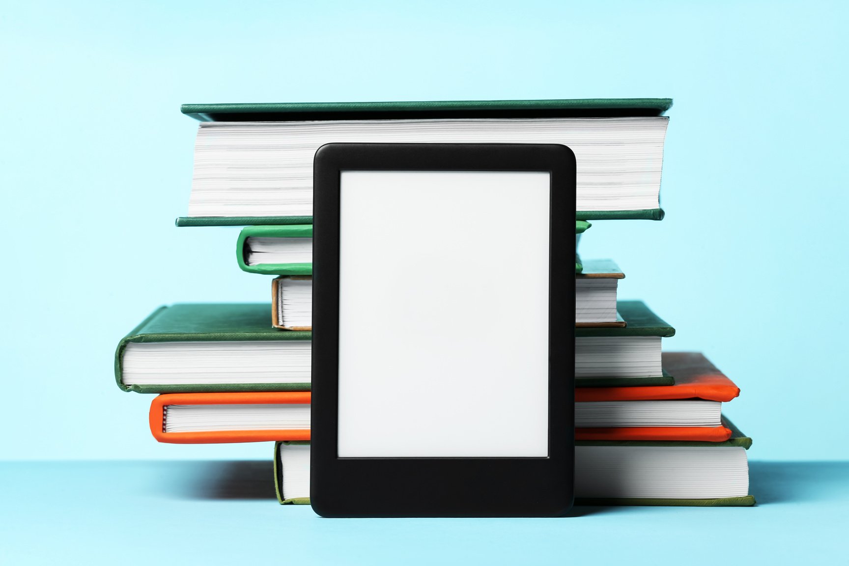 Modern e-book reader and stack of hard cover books on light blue background